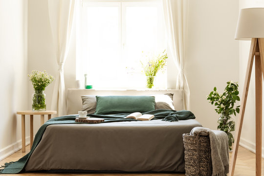 Eco friendly bedroom interior with a bed dressed in gray and green bedding. Sunny window as a background. Real photo.