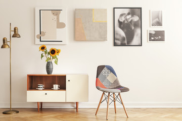 Colorful chair standing in white living room interior with gallery on wall, cupboard with flowers and tea cups in real photo