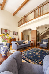 Real photo of a living room interior with blue sofa, rug, porcelain vase with flowers and stairs
