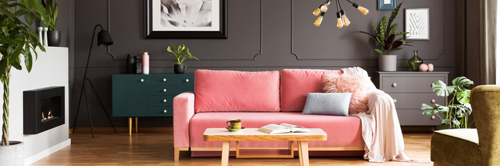 Wooden table in front of pink sofa with blanket in grey living room interior with fireplace. Real...