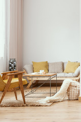 Yellow wooden armchair at table in white living room interior with pillows on sofa. Real photo
