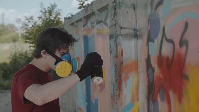 Graffiti master with respirator painting on street wall. 4K