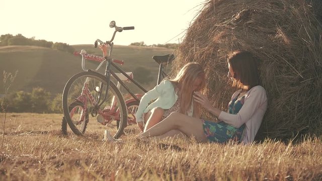 Mother and daughter in a field with hay stack in a sunny day. Family mom with cheerful daughter they came by bicycle in the field. Lifestyle, family holiday, outdoor, concept.