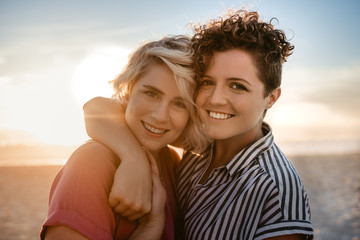 Fototapeta premium Smiling lesbian couple standing together on a beach at sunset
