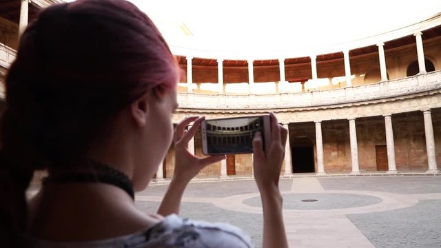 Redhead girl making a photograph with smartphone to a monument in Granada, Spain.