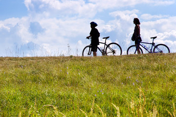 Fototapeta premium unidentifiable bikers on the meadow, Czech republic - silhouette of people with bicycles in the nature