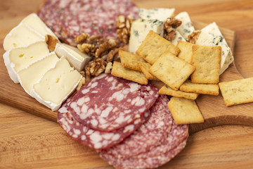 Mix of different snacks and appetizers. Slices of salami , crackers, french camambert, cheese with blue mildew with honey and of walnuts nuts on wooden background.