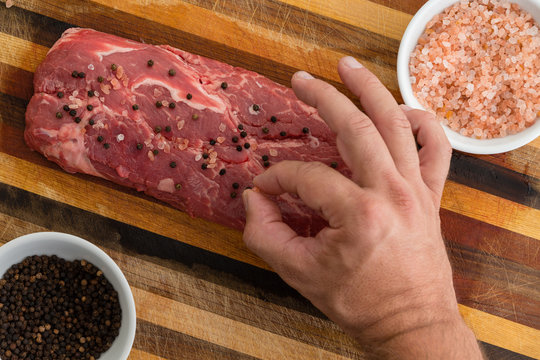 Man dropping seasoning on slab of red meat