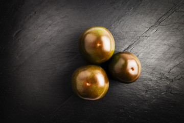 group of dark red kumato tomatoes on a black slate table
