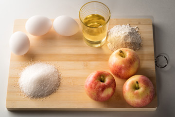 Ingredients for baking apple  pie or cake.Preparing for a Christmas cake with apples.Copy space. Apple, flour, eggs, sugar, sunflower oil, cranberries on a wooden board in daylight in the kitchen.