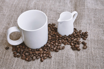An empty white coffee cup with coffee beans on sackcloth background