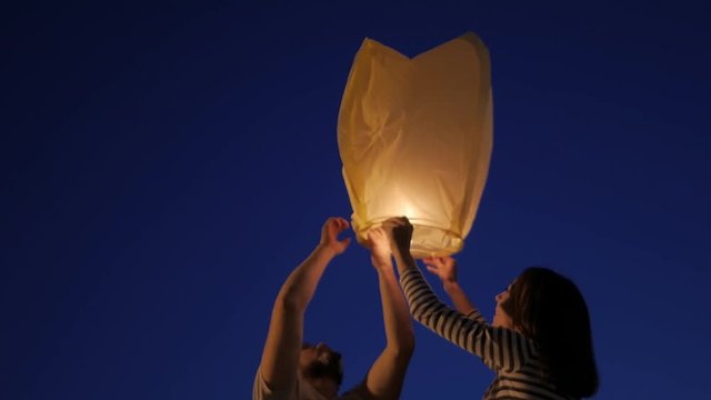 Happy couple launching a Chinese sky fly fire lanterns to make a wish, family.