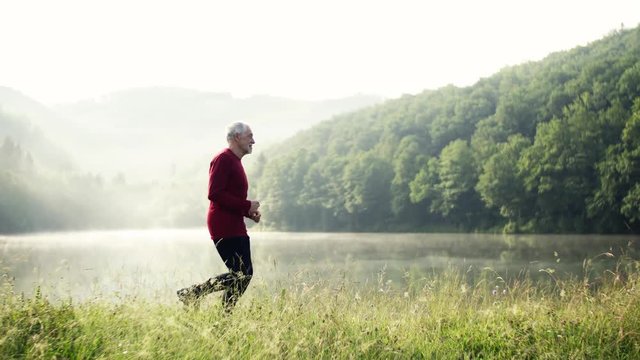 Senior man running by the lake outdoor in foggy morning in nature.