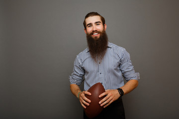 Young cheerful man with a beard holds a rugby ball in his hand.Man is dressed in a blue shirt