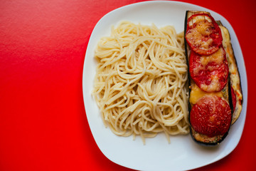 Spaghetti with eggplant and tomatoes with cheese on a white plate. Dish on a red background