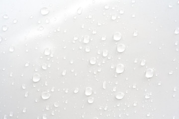 Rain drops on glossy white car hood surface of window at early night in rainy season - nature abstract background