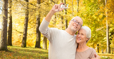 Fototapeta premium age, tourism, travel, technology and people concept - senior couple with camera taking selfie on street