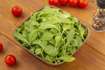 Fresh arugula salad in a bowl, on a wooden background.