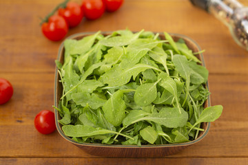 Fresh arugula salad in a bowl, on a wooden background.