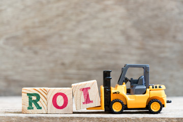 Toy forklift hold letter block  in word ROI (abbreviation of Return on investment) on wood background