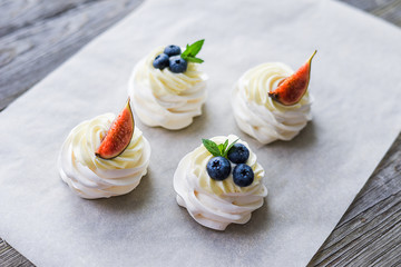 Pavlova meringue cake with figs, blueberries and mint leaves on a wooden background.
