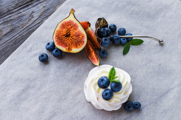 Pavlova meringue cake with figs, blueberries and mint leaves on a wooden background.