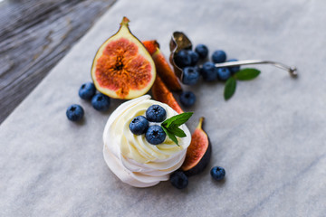 Pavlova meringue cake with figs, blueberries and mint leaves on a wooden background.