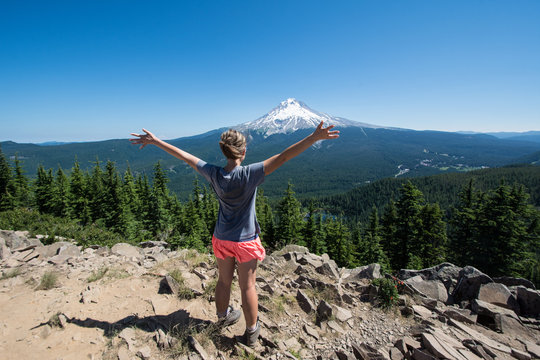 Female hiker stands on the summit of Tom Dick and Harry Mountain in Mt. Hood National Forest, with her arms held up, looking at Mount Hood.
