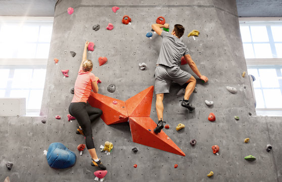 fitness, extreme sport and healthy lifestyle concept - young man and woman bouldering on a rock climbing wall at indoor gym