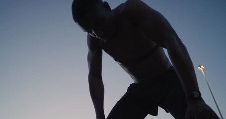 muscular african american runner man resting after intense running exercise exhausted shirtless athlete breathing tired in urban city at night
