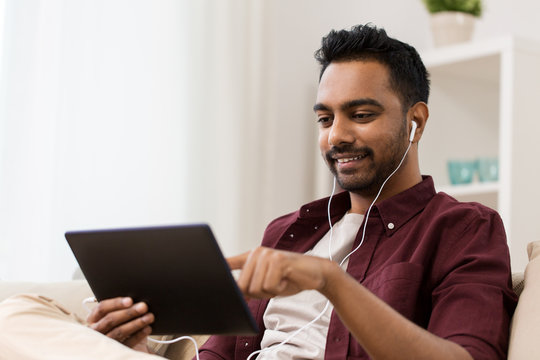 technology, leisure and people concept - happy man in earphones with tablet pc computer listening to music at home