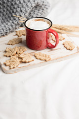 Red Cup of coffee on a bed. Hot drink on sheet, warm cozy grey knitted plaid. Cookies shape of a leaves on a tray. Top view or flat lay, copy space for your text