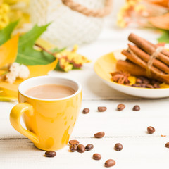 Autumn banner with cup of coffee with cinnamon on white wooden background with colorful tree leaves.