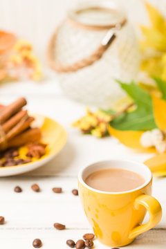 Autumn banner with cup of coffee with cinnamon on white wooden background with colorful tree leaves.
