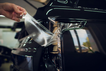 Worker hands installs car paint protection film wrap.