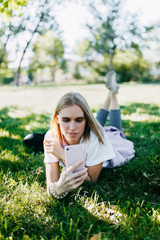 Young woman with phone in the park on green grass. Beauty nature scene with colorful background. Outdoor lifestyle.