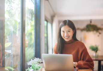 Happy young Asian girl working at a coffee shop with a laptop looking at camera.