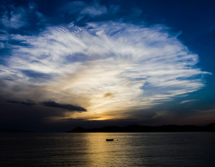 Evening scene of sun setting behind Sipan island, from Lopud, Croatia. Last rays reflecting on the silhouette of a small boat. Light giving a fan-like image of light cloud with blue sky.