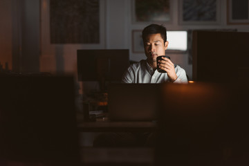 Asian businessman drinking coffee while working late in an offic