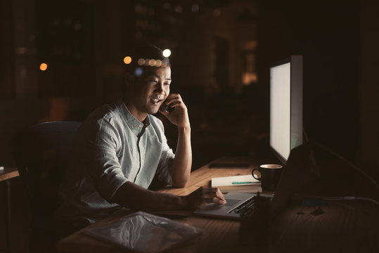 Smiling Asian Businessman Talking On His Cellphone Late At Night