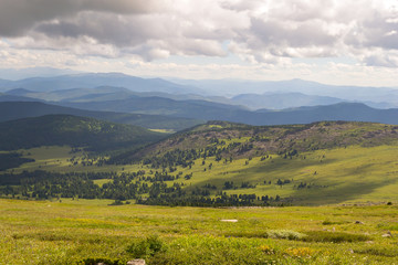 Landscape of green valley flooded with light with lush green grass, mountains, covered with stone and hills, a fresh summer day under a blue sky with white clouds and sun rays in Altai mountains