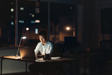 Young Asian businessman working overtime in a dark office - Powered by Adobe
