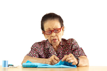 Elder Asian lady age between 80-85 years old is sewing a cloth professionally.