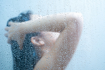 Women showering in the shower room close up with a water drop on glass door.