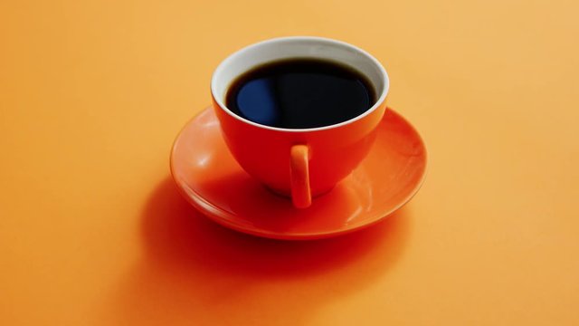 From above view of cup with hot black coffee on orange background