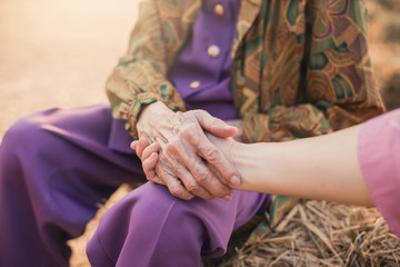 Hands of young adult and senior women. Senior and young holding hands outside.