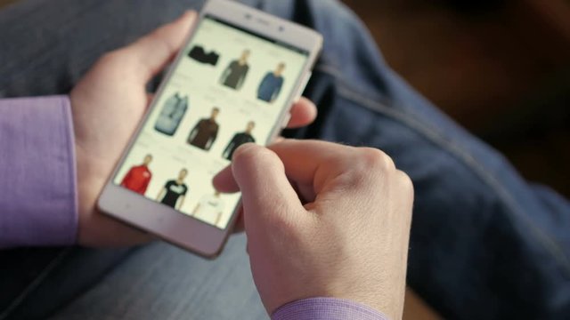 A man looks at the goods in the online clothing store. People using Smartphone, online shopping. The screen is blurred. Close-up. 4K UHD.