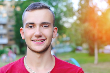 The young man is resting in nature, smiling and on his teeth clearly sees the ceramic white braces