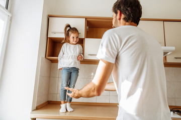 Fototapeta premium Family. Fun. Parenthood. Dad and his little daughter are playing in the kitchen at home