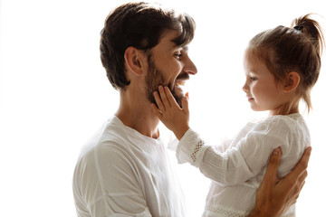 Parenthood. Family. Love. Dad is holding his little daughter in his arms and smiling. Girl is touching dad's beard. On white background